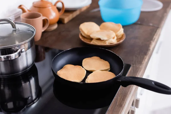 Selective focus of pancakes on frying pan on stove in kitchen — Stock Photo
