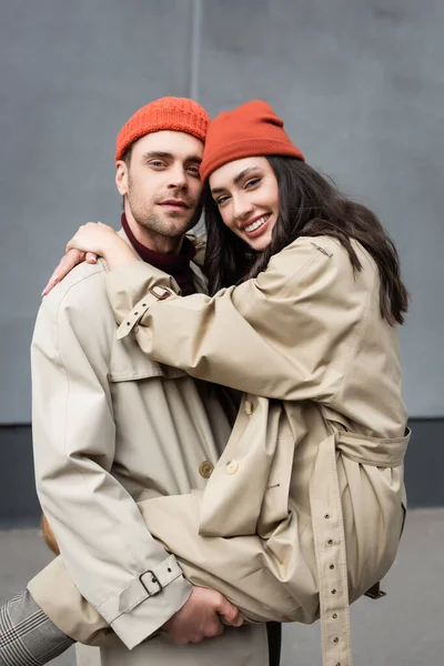 Elegante hombre sosteniendo en brazos mujer en gorro sombrero y gabardina - foto de stock