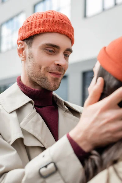 Selektiver Fokus eines zufriedenen Mannes, der junge Frau in Mütze berührt — Stockfoto