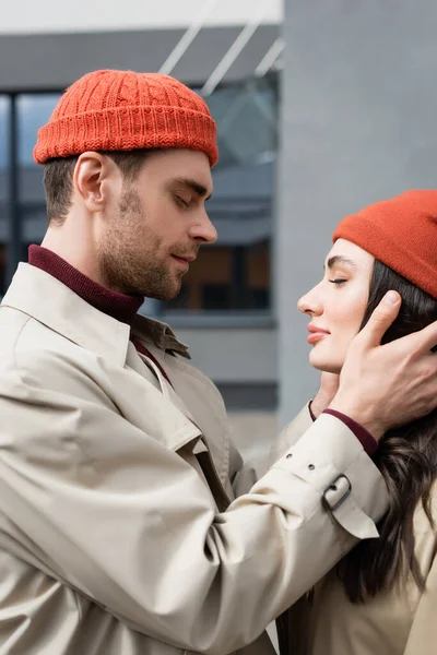 Vista lateral del hombre de moda tocando a la mujer joven en gorro sombrero - foto de stock