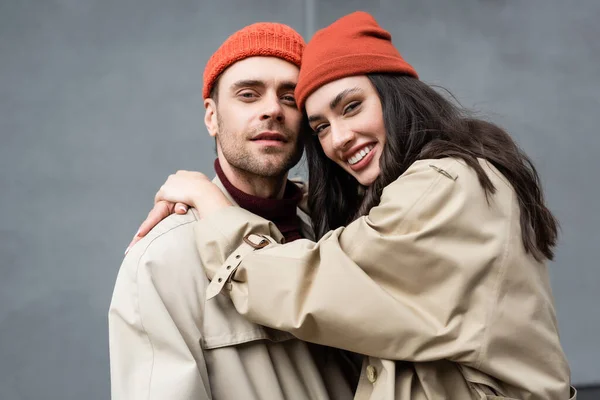 Trendy woman in beanie hat hugging man in trench coat — Stock Photo