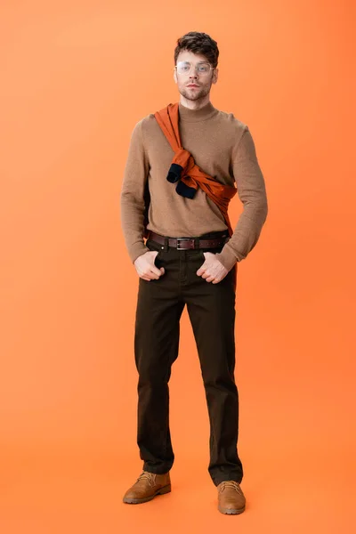 Full length of stylish man in glasses standing with hands in pockets on orange — Stock Photo