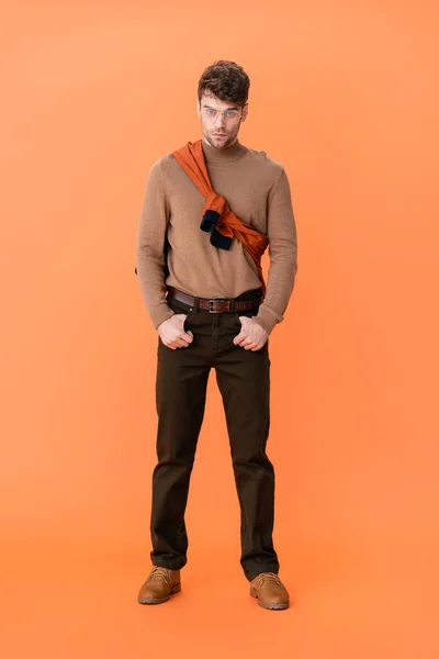 Stylischer Mann in Brille und Herbstoutfit mit Händen in Taschen auf orange — Stockfoto