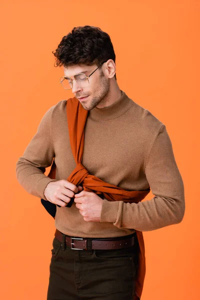 Trendy man in glasses touching jumper and looking away isolated on orange — Stock Photo