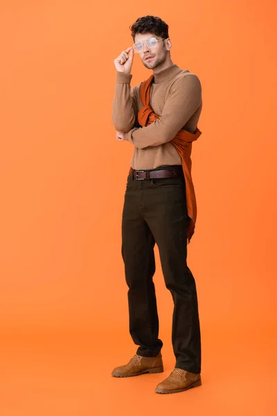 Full length of trendy man in autumn outfit touching glasses on orange — Stock Photo