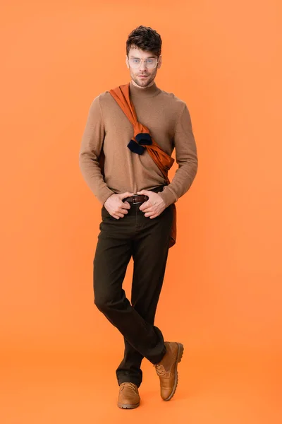 Hombre de moda en traje de otoño y gafas de pie con las piernas cruzadas en naranja - foto de stock