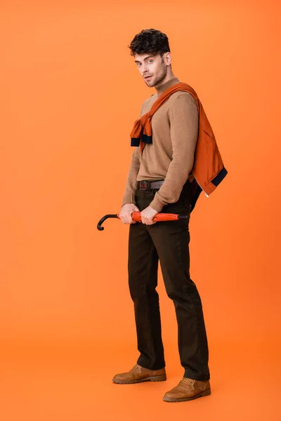 Полная длина модный человек в осеннем наряде держа зонтик на оранжевом — стоковое фото
