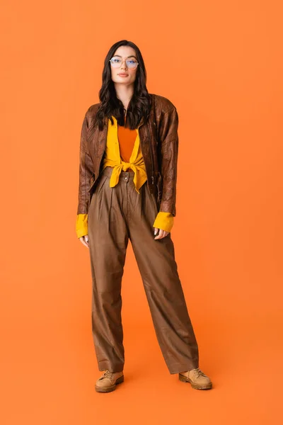 Longitud completa de la mujer con estilo en traje de otoño y gafas de pie en naranja - foto de stock