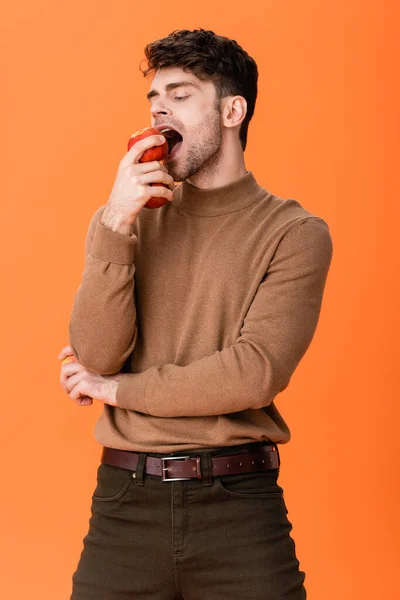 Man in autumn outfit eating fresh apple isolated on orange — Stock Photo