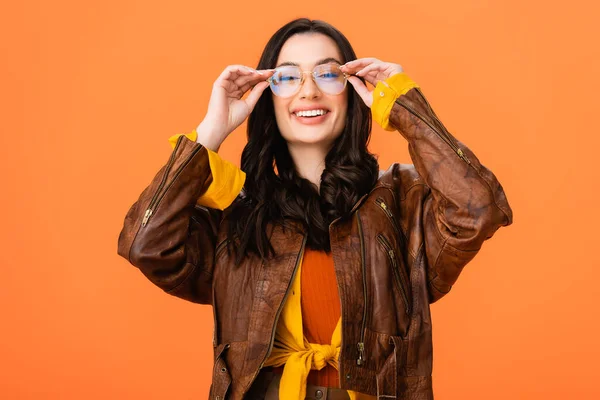 Стильна жінка в осінньому вбранні торкається окулярів ізольовано на помаранчевому — стокове фото