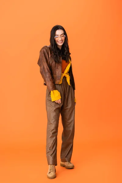 Longueur totale de la jeune femme en tenue d'automne et des lunettes debout sur orange — Photo de stock