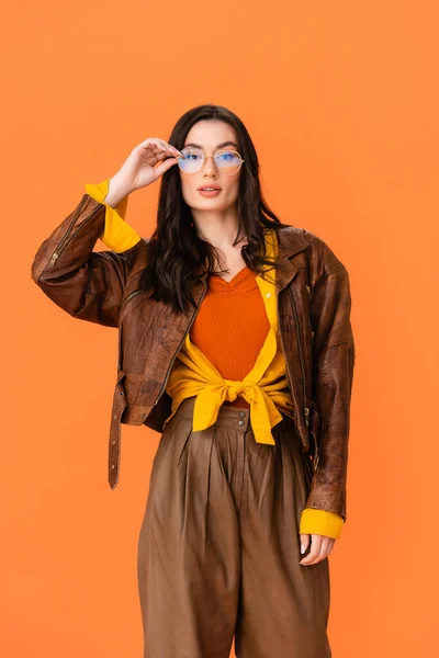 Jeune femme en tenue d'automne regardant caméra et lunettes touchantes isolées sur orange — Photo de stock