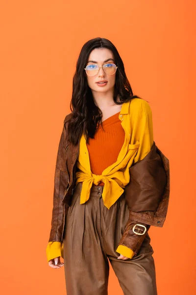 Mujer joven en traje de otoño y gafas mirando a la cámara aislada en naranja - foto de stock