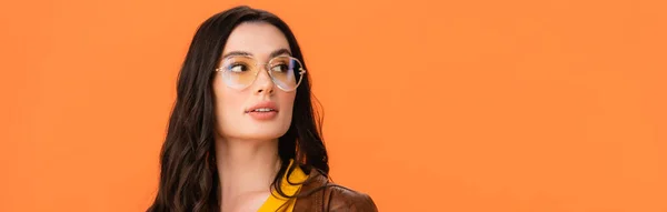 Cultivo panorámico de mujer joven en gafas mirando hacia otro lado aislado en naranja - foto de stock