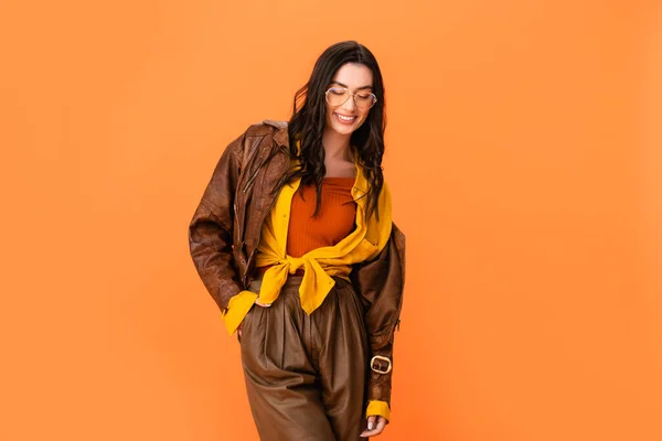 Молода жінка в осінньому вбранні стоїть з рукою в кишені і дивиться вниз ізольовано на помаранчевому — стокове фото