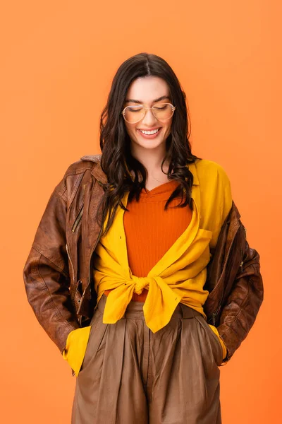 Mujer joven en traje de otoño de pie con las manos en los bolsillos y mirando hacia abajo aislado en naranja - foto de stock