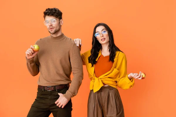 Trendy couple in glasses and autumn outfit holding apples isolated on orange — Stock Photo