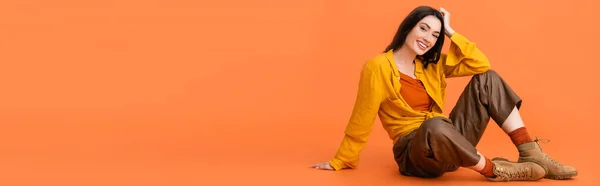 Панорамна концепція брюнетки і модна жінка в осінньому вбранні, сидячи на помаранчевому — стокове фото