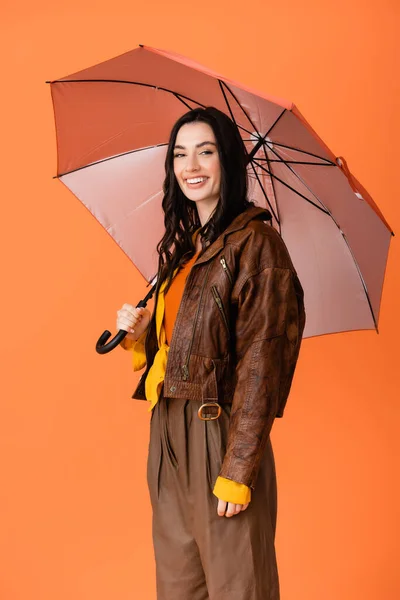 Young woman in autumn outfit standing under umbrella isolated on orange — Stock Photo