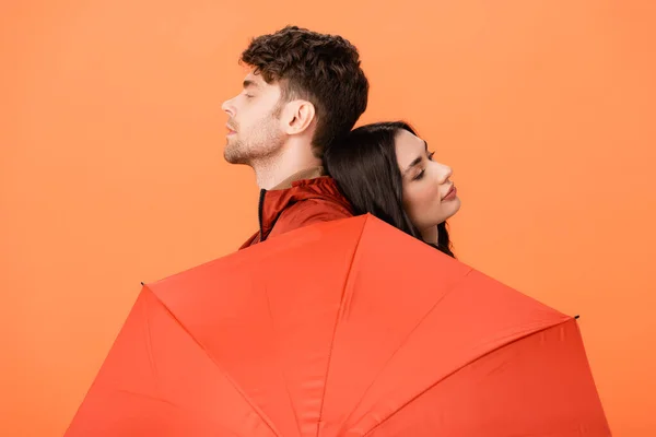 Hombre y mujer de moda cerca de paraguas aislado en naranja - foto de stock