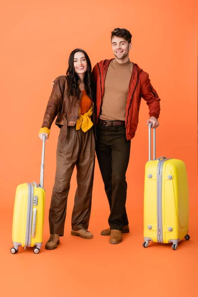 Full length of stylish couple in autumn outfit standing near yellow baggage on orange — Stock Photo