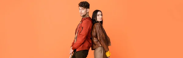 Panoramic shot of fashionable man and woman standing back to back isolated on orange — Stock Photo