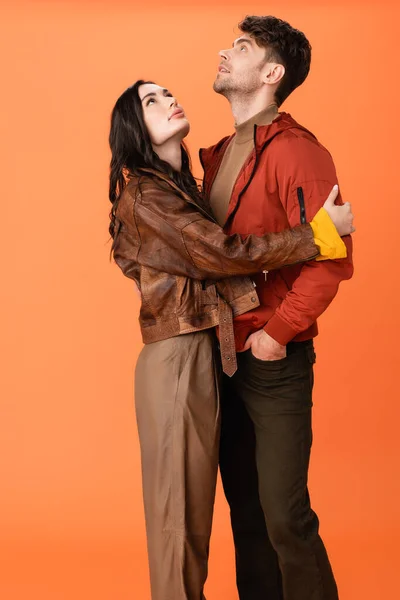 Brunette woman hugging stylish man standing with hand in pocket and looking up on orange — Stock Photo