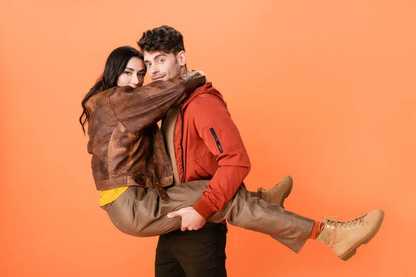 Trendy man holding in arms woman in autumn outfit on orange — Stock Photo