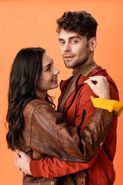 Joven morena mujer abrazando elegante hombre en chaqueta aislado en naranja - foto de stock