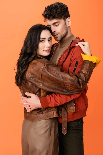 Модна пара в шкіряних куртках обіймається ізольовано на помаранчевому — стокове фото