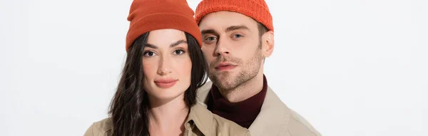 Orientação panorâmica do casal na moda em chapéus beanie olhando para a câmera isolada no branco — Fotografia de Stock