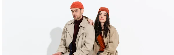 Colpo panoramico di donna elegante in trench vicino uomo alla moda in cappello beanie su bianco — Foto stock