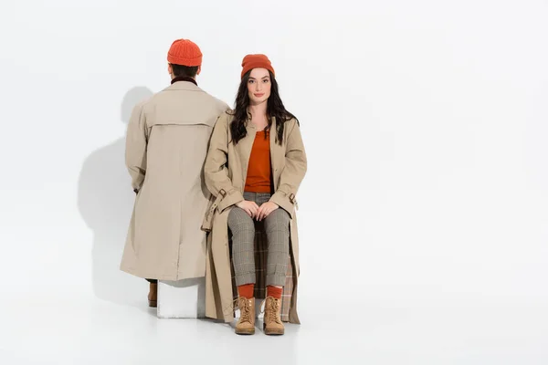 Mujer elegante sentado cerca de hombre en gorro sombrero en blanco - foto de stock