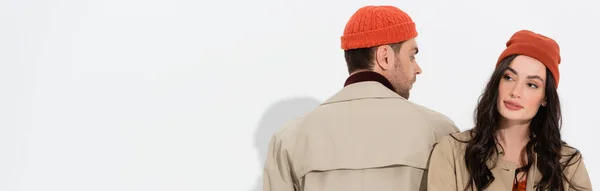 Horizontal image of stylish man in trench coat looking at woman in beanie hat on white — Stock Photo