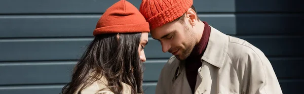 Panoramic crop of stylish couple in hats leaning on each other outside — Stock Photo