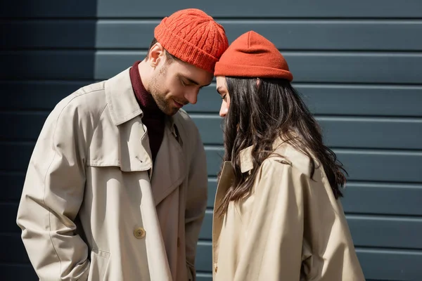 Stylish couple in trench coats and hats leaning on each other outside — Stock Photo