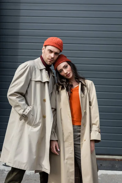 Uomo alla moda in trench e cappello in piedi con mano in tasca vicino alla donna fuori — Foto stock
