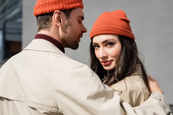 Homem elegante em casaco de trincheira abraçando mulher em chapéu gorro fora — Fotografia de Stock