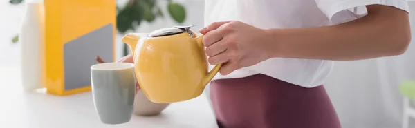 Vista recortada de ama de casa joven verter té en la taza, encabezado del sitio web - foto de stock