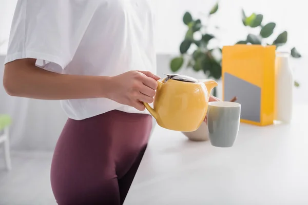 Abgeschnittene Ansicht einer jungen Frau, die Tee aus Teekanne in der Küche einschenkt — Stockfoto