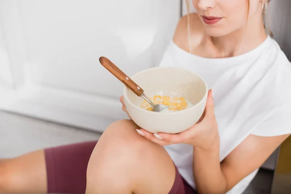 Abgeschnittene Ansicht einer jungen Frau, die mit einer Schale Cornflakes auf dem Boden sitzt — Stockfoto