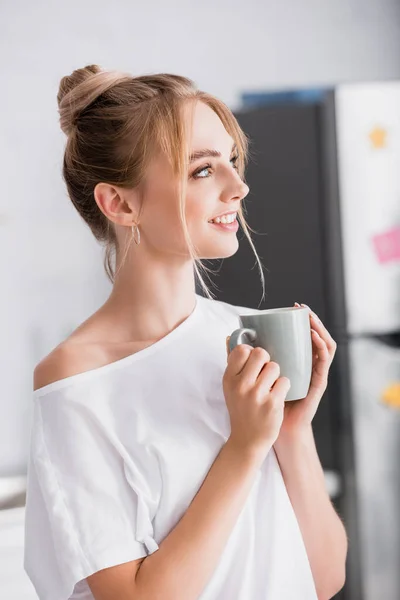 Lächelnde blonde Frau schaut weg, während sie eine Tasse Tee in der Hand hält — Stockfoto