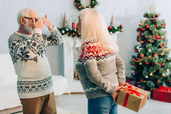 Senior man covering eyes with hands while wife holding present behind back — Stock Photo