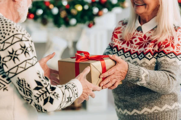 Ausgeschnittene Ansicht einer lächelnden Seniorin, die ihrem Mann eine Geschenkbox überreicht — Stockfoto