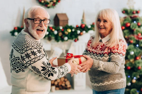 Happy senior woman presenting christmas gift to excited husband — Stock Photo