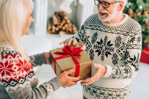 Excited senior man in eyeglasses taking christmas present from smiling wife — Stock Photo