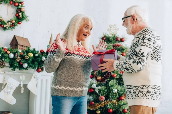 Uomo anziano che presenta il regalo di Natale alla moglie eccitata a casa — Foto stock