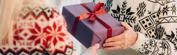 Cropped view of senior man presenting christmas gift to wife, panoramic concept — Stock Photo