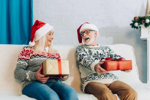 Aufgeregtes Senioren-Paar schaut sich auf Sofa mit Geschenkschachteln an — Stockfoto