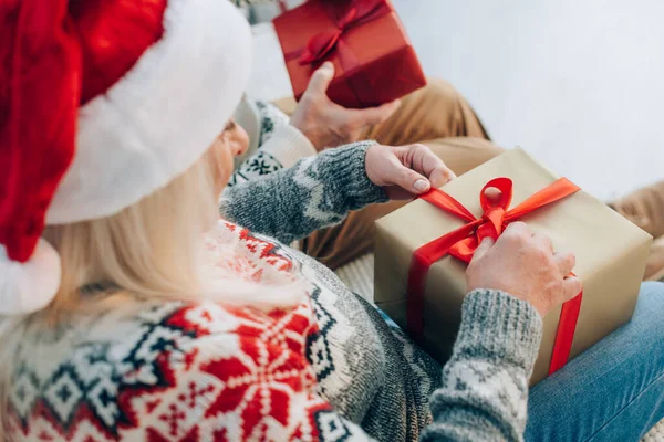 Selektiver Fokus der Seniorin im Weihnachtsmannhut beim Öffnen der Geschenkbox in der Nähe ihres Ehemannes — Stockfoto